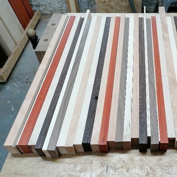 Holzstreifen aus verschiedenfarbigen Holzarten liegen nebeneinander in der Werkstatt